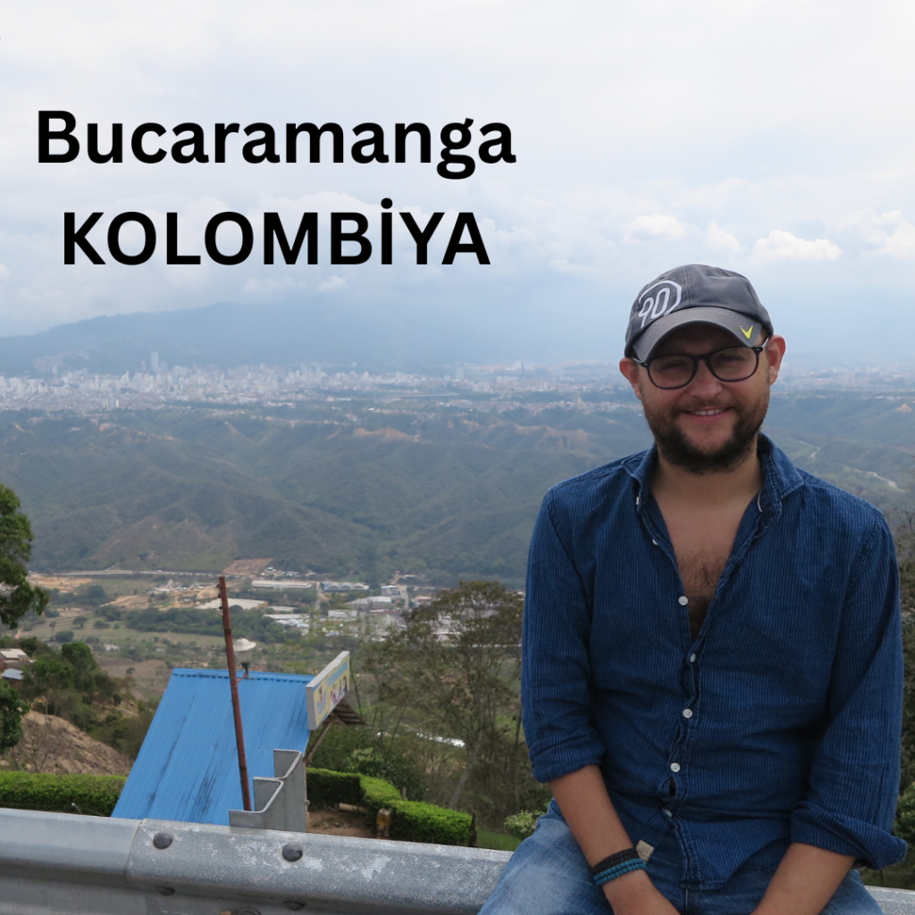 Arka planda yemyeşil dağlar ve bulutlu bir gökyüzü ile Kolombiya, Bucaramanga'nın panoramik manzarası önünde gülümseyen bir adam.