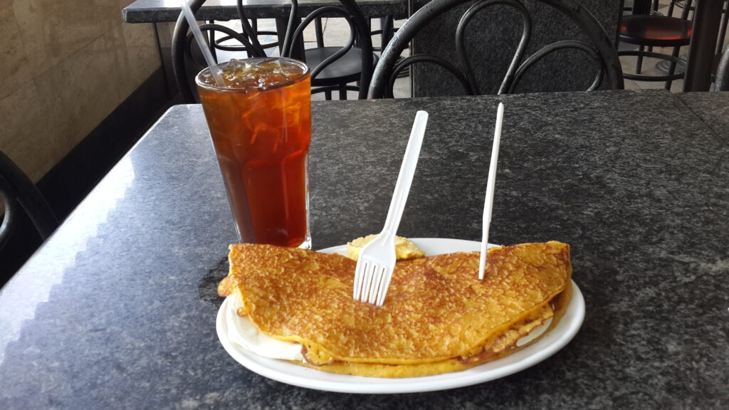 Taze mısırdan yapılan Venezuelalı cachapa; erimiş beyaz peynir dolgulu, kafede buzlu çay eşliğinde servis edilmiş.