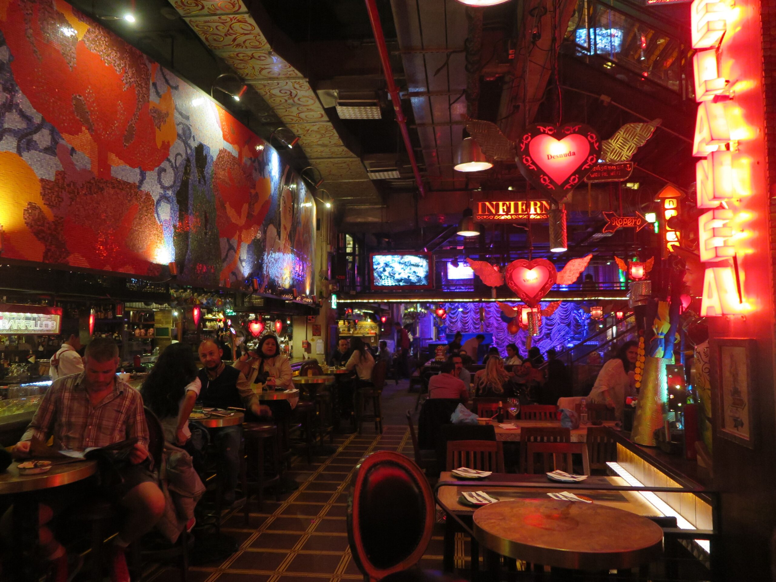 Colorful interior of Andrés Carne de Res (Andrés D.C.) in Bogotá, with neon heart signs, vibrant murals, warm red lighting, and guests dining at tables and the bar.