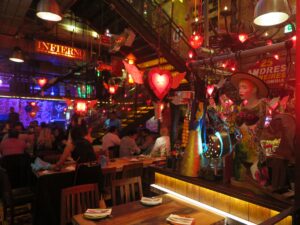 Interior of Andrés Carne de Res (Andrés D.C.) in Bogotá, filled with glowing red heart-shaped neon lights, eclectic décor, a colorful statue, and guests dining at wooden tables.