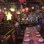 Dining area inside Andrés Carne de Res (Andrés D.C.) in Bogotá, featuring long wooden tables set with plates, a large illuminated star decoration, red signage, and guests seated near the bar.