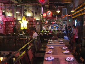 Dining area inside Andrés Carne de Res (Andrés D.C.) in Bogotá, featuring long wooden tables set with plates, a large illuminated star decoration, red signage, and guests seated near the bar.