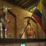 Quirky interior decor at Andrés Carne de Res in Bogota featuring a silver cow statue and a religious figure with a red heart on a brick wall.