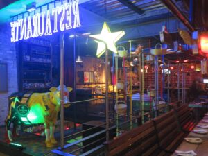 Vibrant interior of Andrés Carne de Res (Andrés D.C.) in Bogota featuring neon signs, a glowing yellow cow statue, and hanging baskets.