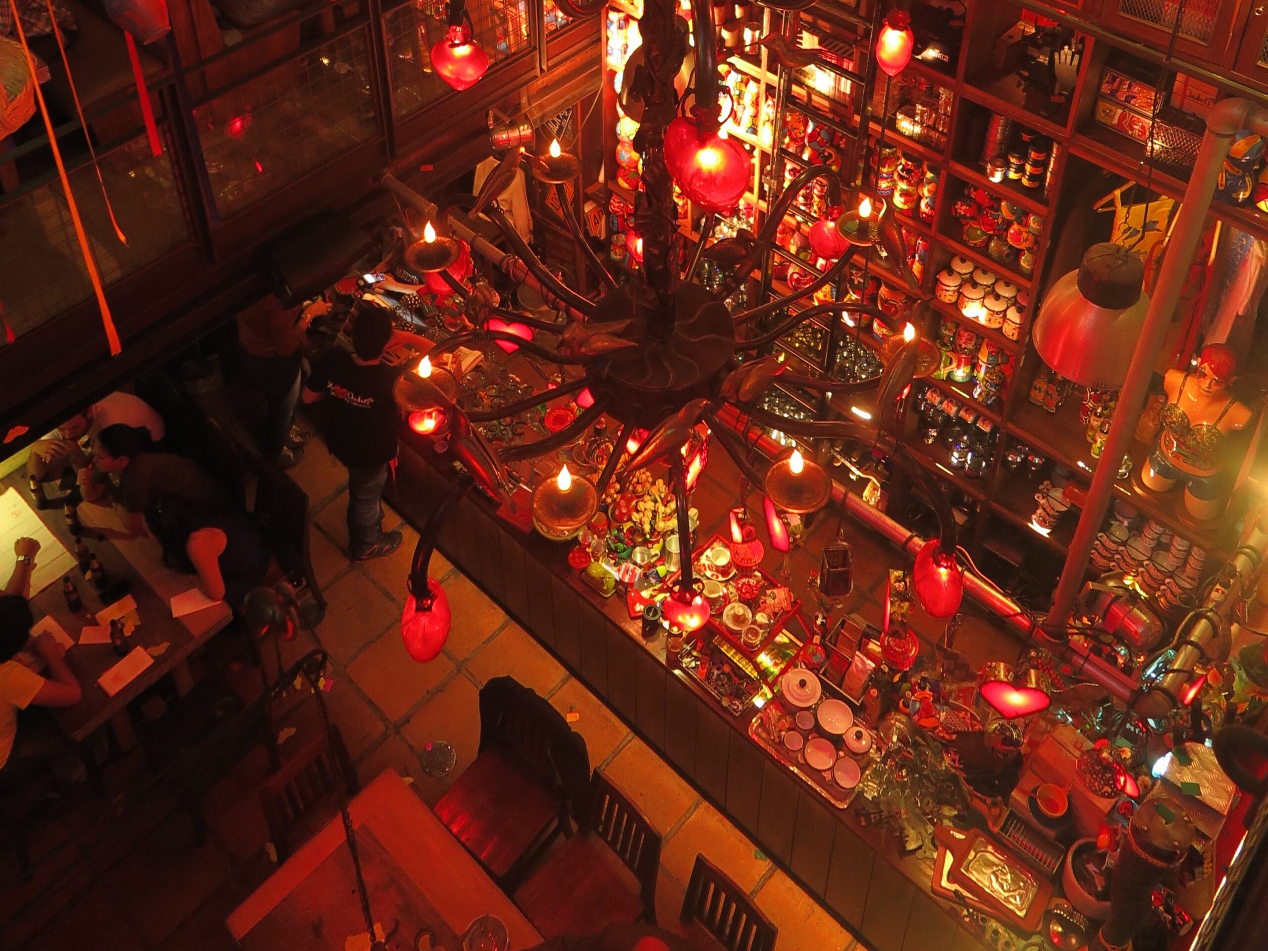 High-angle view of a crowded bar area in Andrés Carne de Res Bogota, featuring large red heart-shaped lanterns and an ornate chandelier.