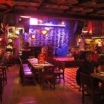 Interior view of Andrés Carne de Res in Bogota featuring a dining area with wooden tables, a checkered floor, and a stage with purple curtains and heart decorations.