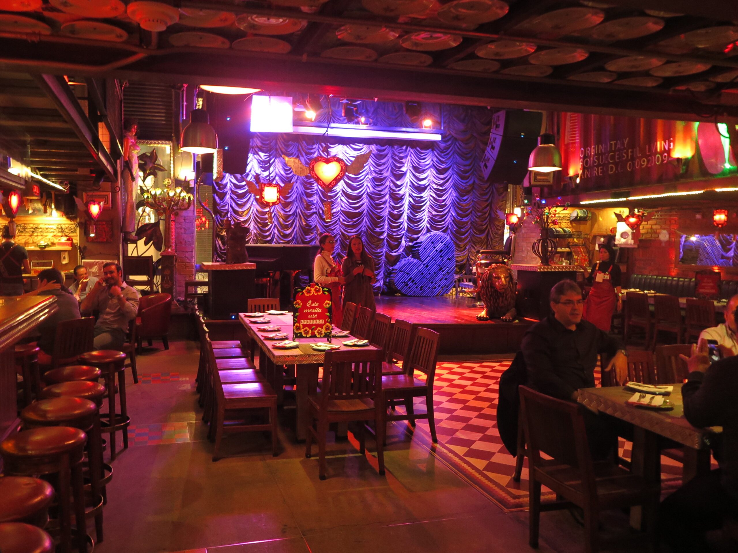 Interior view of Andrés Carne de Res in Bogota featuring a dining area with wooden tables, a checkered floor, and a stage with purple curtains and heart decorations.