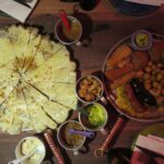 Top-down view of a traditional Colombian meal at Andrés Carne de Res, featuring a large cheesy arepa de choclo, grilled meats, sausages, and various side dipping sauces.