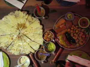 Top-down view of a traditional Colombian meal at Andrés Carne de Res, featuring a large cheesy arepa de choclo, grilled meats, sausages, and various side dipping sauces.