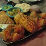 Close-up of a Colombian appetizer platter at Andrés Carne de Res featuring grilled corn on the cob, papas criollas with hogao sauce, an arepa, and bowls of guacamole and salsa.