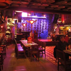 Interior view of Andrés Carne de Res in Bogota featuring a dining area with wooden tables, a checkered floor, and a stage with purple curtains and heart decorations.