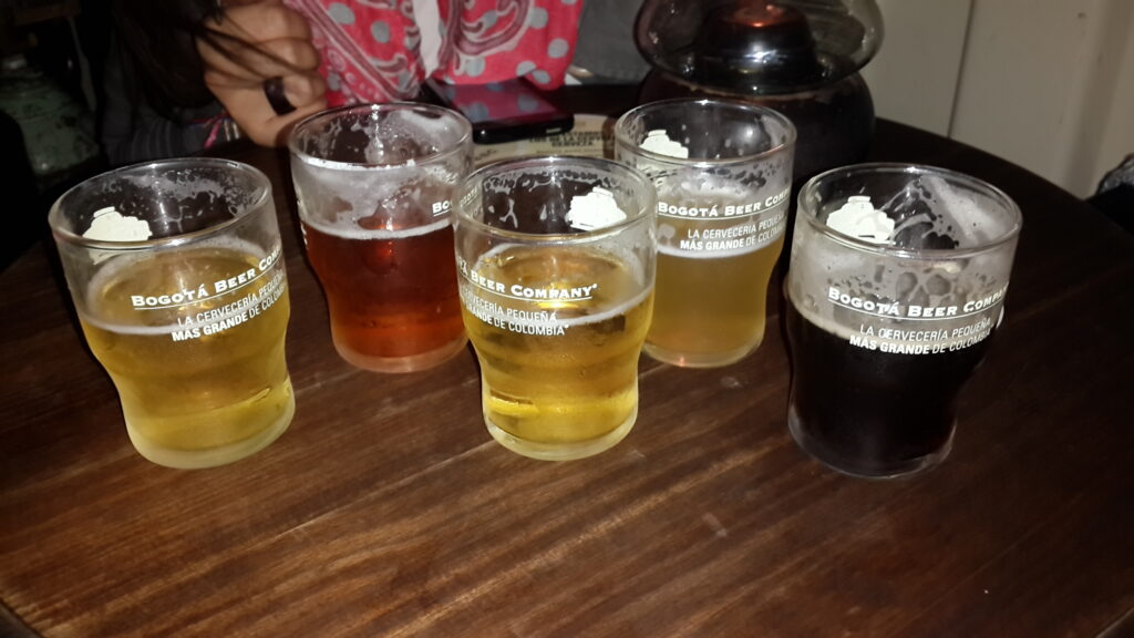 Bogota BBC A wooden table with five different glasses of craft beer from Bogota Beer Company (BBC), ranging from light lager to dark stout.
