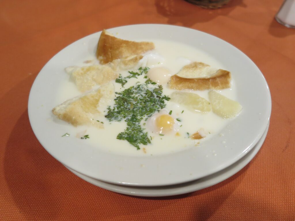 Bogota Changua A bowl of traditional Changua, a Colombian milk-based breakfast soup, featuring poached eggs, pieces of bread, and a generous sprinkle of fresh green cilantro on top.