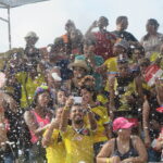 A large, jubilant crowd in Cartagena, Colombia, celebrating Independence Day while being sprayed with white foam. Many people are wearing yellow Colombian football jerseys.