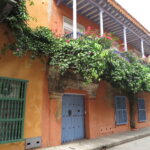 Close-up of an orange colonial house in Cartagena with a purple balcony and thick green vines.