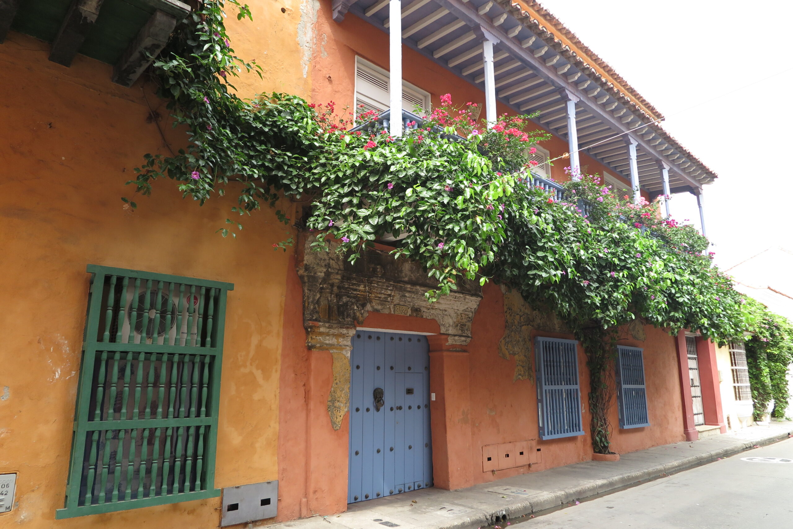 Close-up of an orange colonial house in Cartagena with a purple balcony and thick green vines.