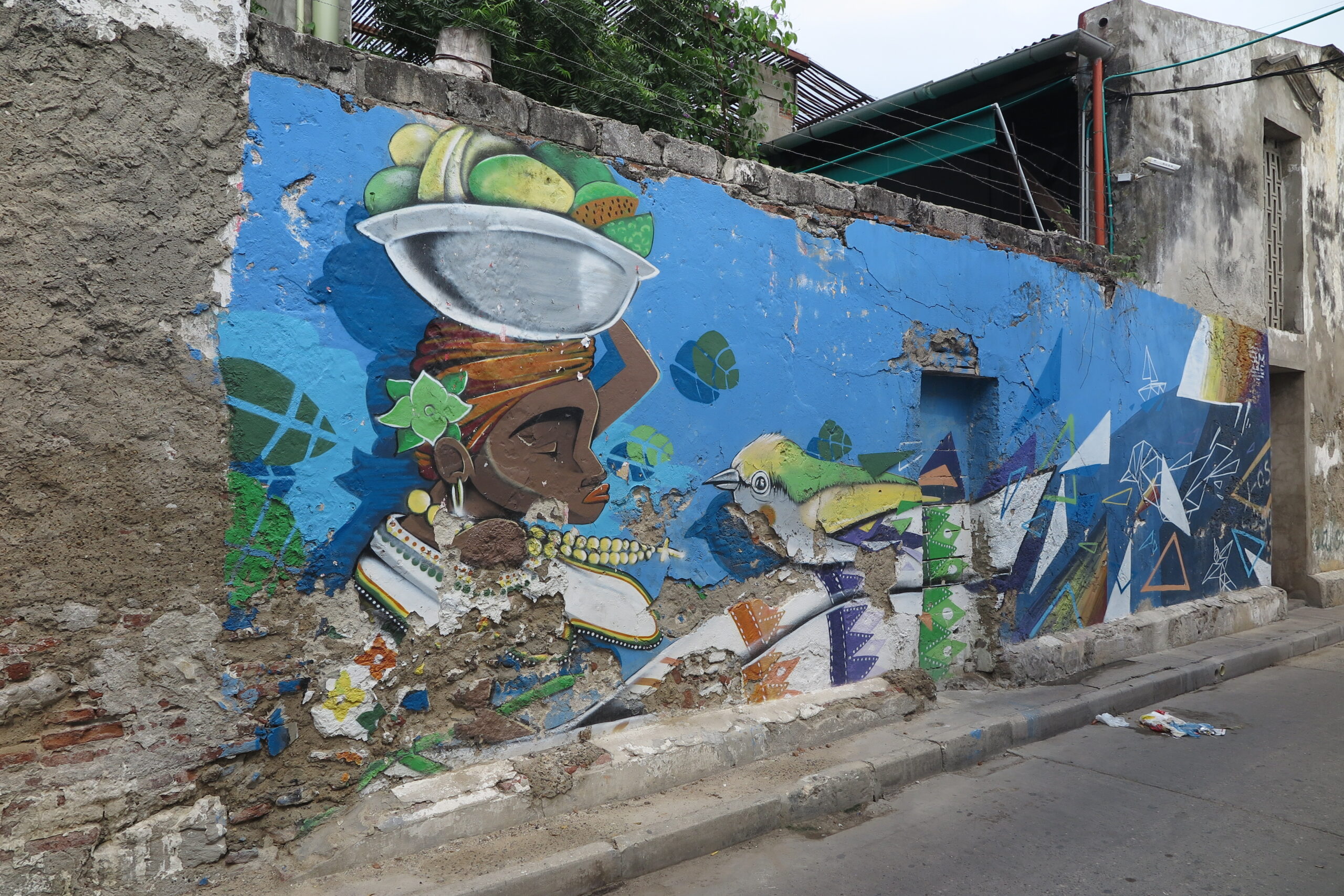 A colorful wall mural in Cartagena depicting a Palenquera woman carrying fruit on her head.
