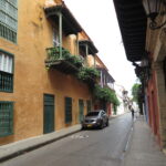An orange colonial building with green shutters and balconies overlooking a quiet street with a parked car.