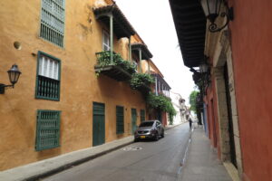 An orange colonial building with green shutters and balconies overlooking a quiet street with a parked car.
