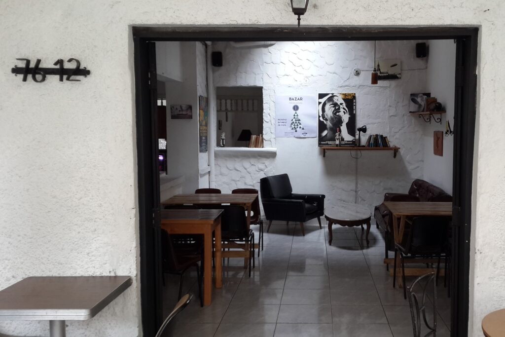 Medellin Cafe Zeppelin A view through a doorway into the interior of Café Zeppelin in Medellin. The room has white textured walls, wooden tables with dark chairs, a black leather armchair, and posters on the wall, including one of a jazz musician.