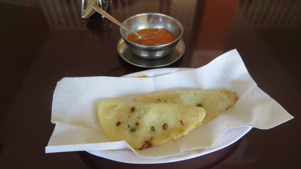 Two golden-brown, crispy Empanadas de Morocho served on a white paper napkin over a white plate, with a metal bowl of spicy ají sauce in the background on a dark table.