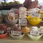 A vibrant display of various bulk spices, herbs, and roots at a market stall in Mercado Amazonas, Ibarra, Ecuador, with hand-written labels such as Ajo Molido, Linaza, and Jengibre.