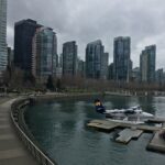 A Harbour Air seaplane moored at a floating dock in Vancouver's Coal Harbour with modern skyscrapers in the background.