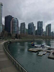 A Harbour Air seaplane moored at a floating dock in Vancouver's Coal Harbour with modern skyscrapers in the background.