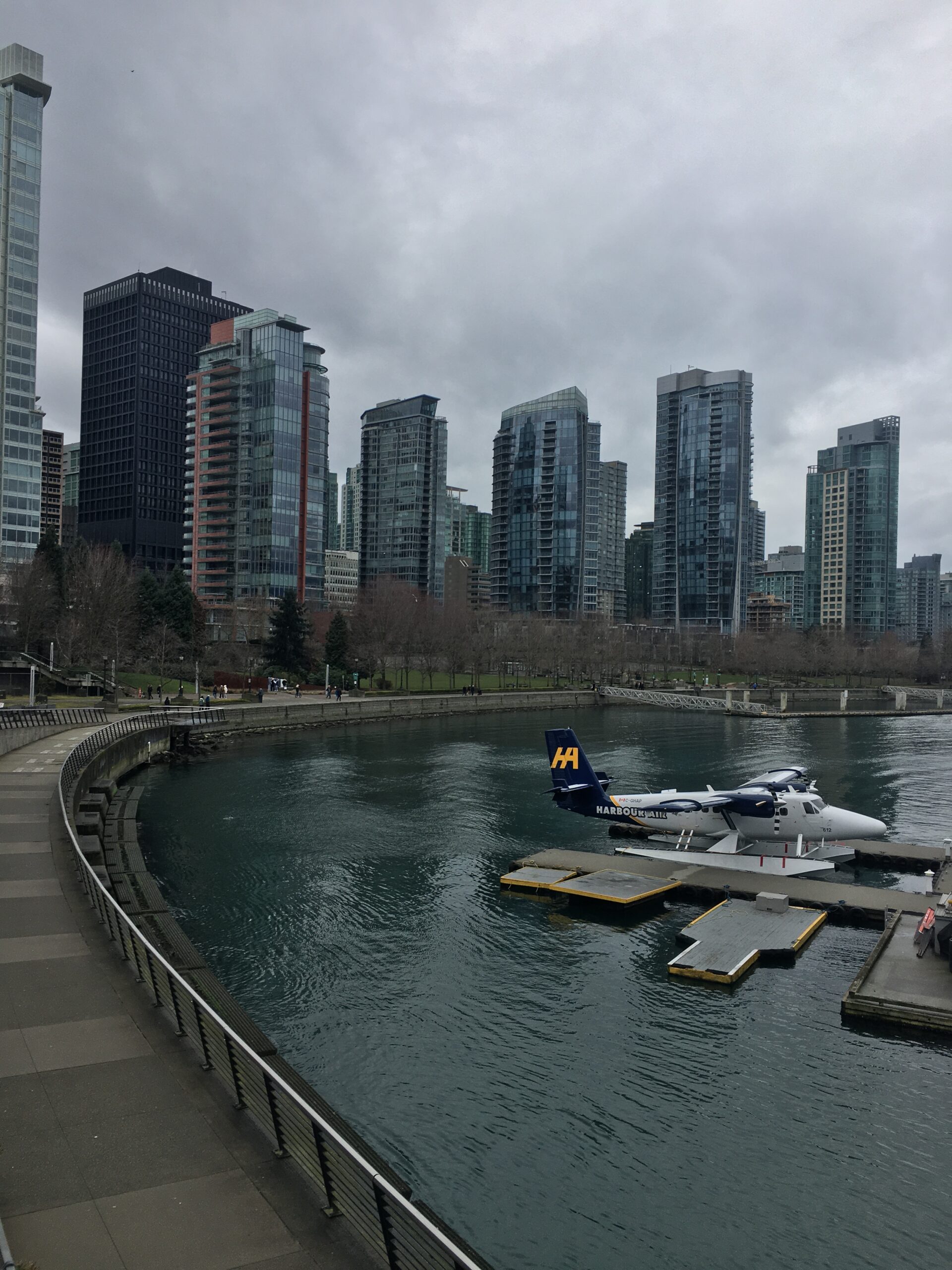 A Harbour Air seaplane moored at a floating dock in Vancouver's Coal Harbour with modern skyscrapers in the background.