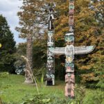Vancouver, BC'deki Stanley Park'ta çimenli bir yamaçta dimdik yükselen üç büyük, parlak boyalı yerli totem direği. Bulutlu bir gökyüzü altında yeşil ve turuncu sonbahar yapraklarına sahip çeşitli ağaçlarla çevrilidirler. Ön plandaki ana direk, kanatlarını açmış bir Gök Gürültüsü Kuşu'nu tasvir etmektedir.