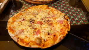 Ekvador'un Quito şehrindeki Café San Blas'ta, koyu renkli ahşap bir masa üzerinde erimiş peynir, mantar ve jambonlu taze pişmiş taş fırın pizzası.