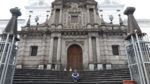A traveler sitting on the stone steps leading up to the grand stone facade of the historic Iglesia de San Francisco in Quito, Ecuador.