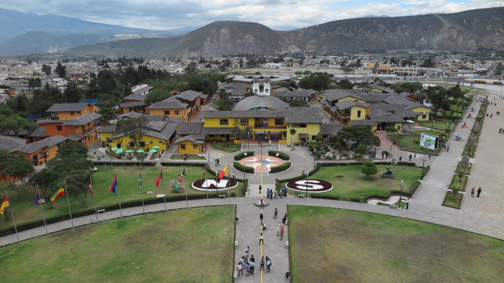A high-angle aerial view of the Mitad del Mundo (Equator Line) tourist village in Quito, Ecuador, showing a yellow line splitting the complex into Northern and Southern hemispheres.