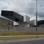 The futuristic UNASUR building with a massive, dramatic cantilever structure at the entrance of Mitad del Mundo (Equator Line) in Quito, Ecuador, under a cloudy sky.