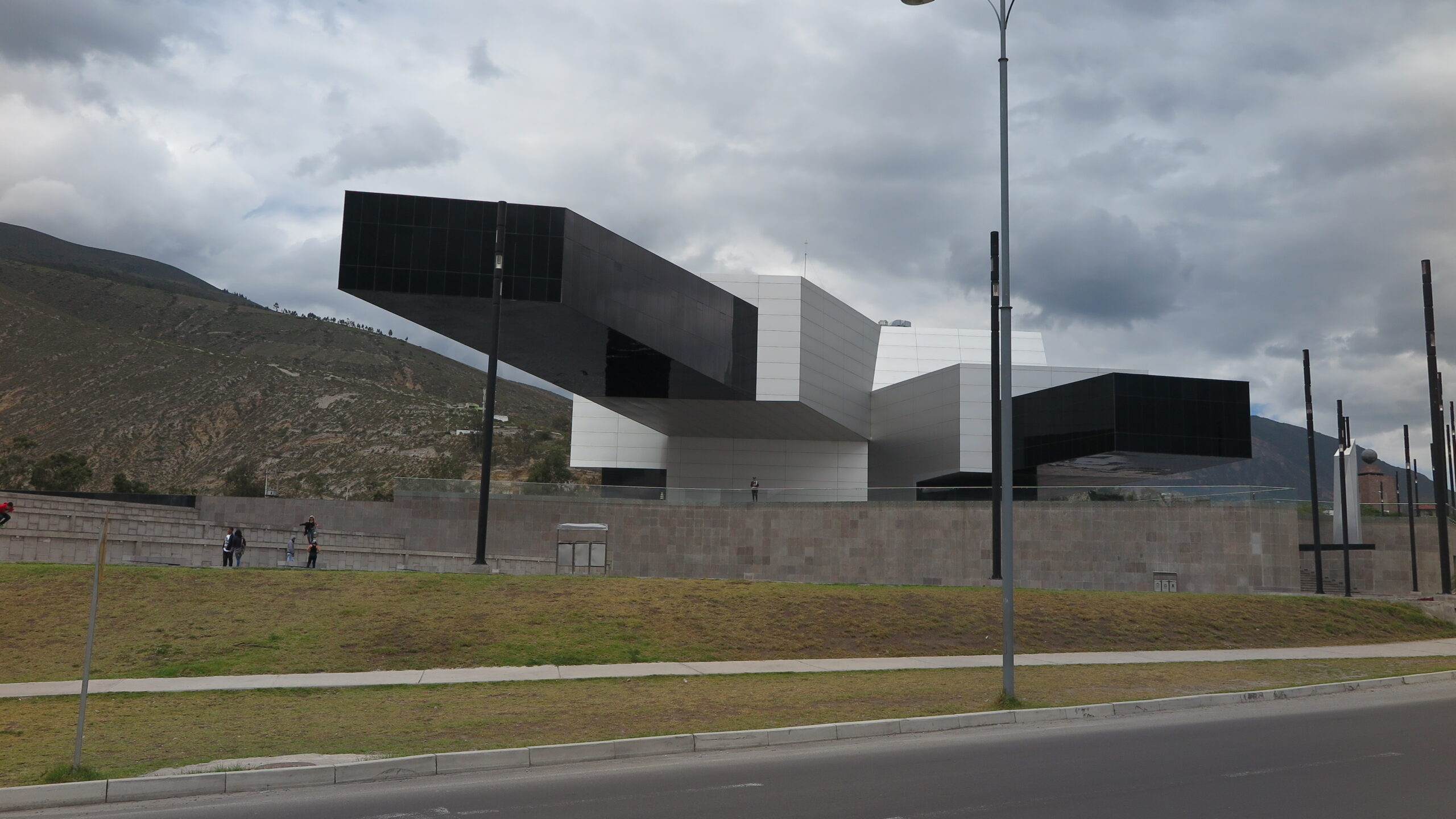 The futuristic UNASUR building with a massive, dramatic cantilever structure at the entrance of Mitad del Mundo (Equator Line) in Quito, Ecuador, under a cloudy sky.
