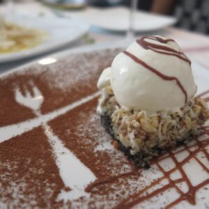 Coconut and chocolate dessert topped with vanilla ice cream, served on a white plate artisticly decorated with cocoa powder fork and knife silhouettes at Platillos Voladores.
