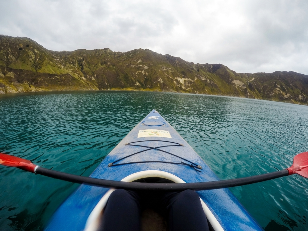 Ecuador Laguna de Quilotoa Kayak A point-of-view (POV) photo from inside a blue kayak, looking across the turquoise water of Laguna de Quilotoa toward the steep, rugged mountain crater walls.