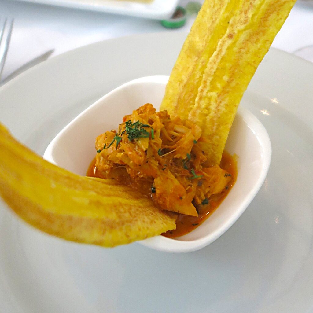 Encocado Platillos Voladores Cali Colombia A closeup photo of a small white bowl filled with Colombia's Pacific coast specialty, Encocado (seafood in coconut milk sauce), garnished with cilantro and served with two large plantain chips at Platillos Voladores restaurant in Cali.