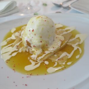 Unique passion fruit shell dessert topped with vanilla ice cream, passion fruit jam, cream drizzle, and crushed pink peppercorns at Platillos Voladores Restaurant.