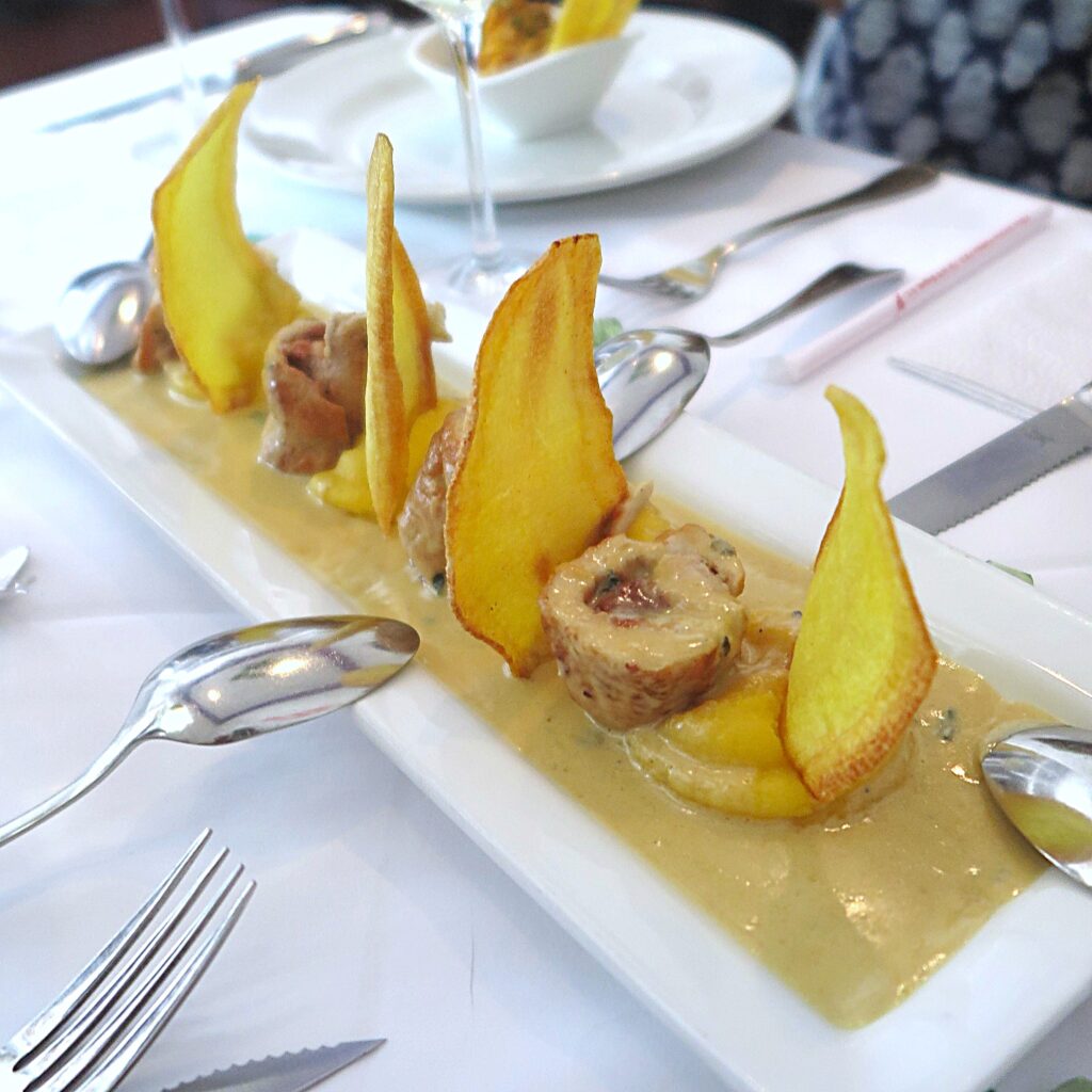 Pollo Guayaba Platillos Voladores Cali Colombia Pollo Guayaba dish at Platillos Voladores restaurant in Cali, Colombia, featuring tender chicken rolls and crispy yellow potato chips on a bed of creamy sauce.