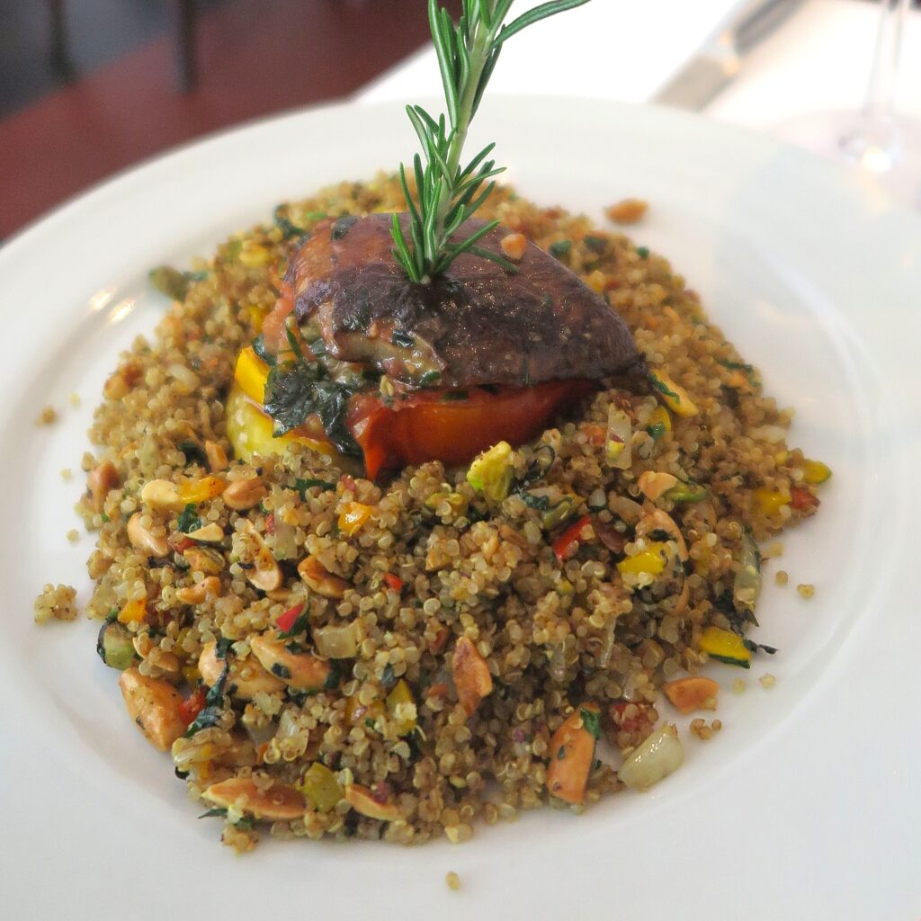 Quinoa Platillos Voladores Restaurant Cali Colombia A gourmet vegetarian quinoa dish mixed with seasonal vegetables, plantains, and roasted peanuts, topped with a stuffed portobello mushroom and a fresh sprig of rosemary.
