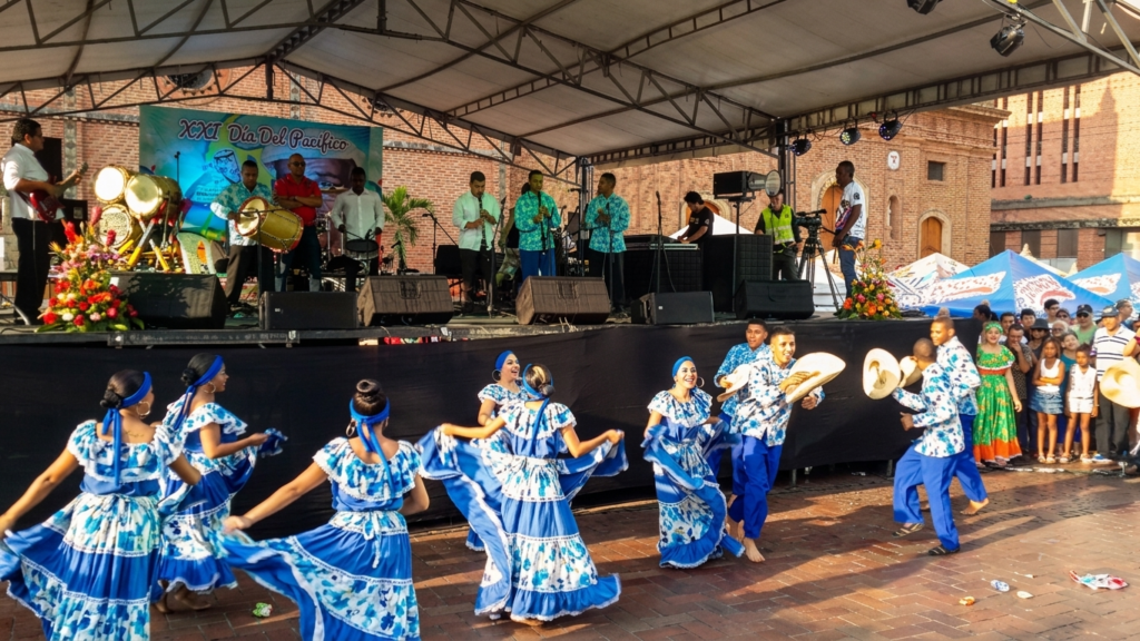 Salsa in Cali Colombia 2 A wide-angle photo captures a group of vibrant salsa dancers in matching blue outfits performing on an outdoor stage in Cali, Colombia. In the background, a band with instruments is visible, all under a canopy structure. This image effectively represents salsa in Cali, highlighting the city's lively dance culture.