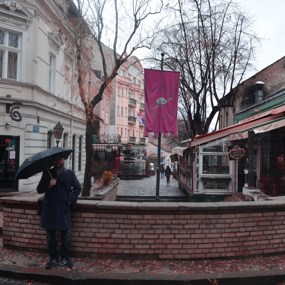 Things to do in Belgrade - A traveler holding an umbrella in front of the iconic Skadarlija street sign in the bohemian quarter of Belgrade, Serbia.