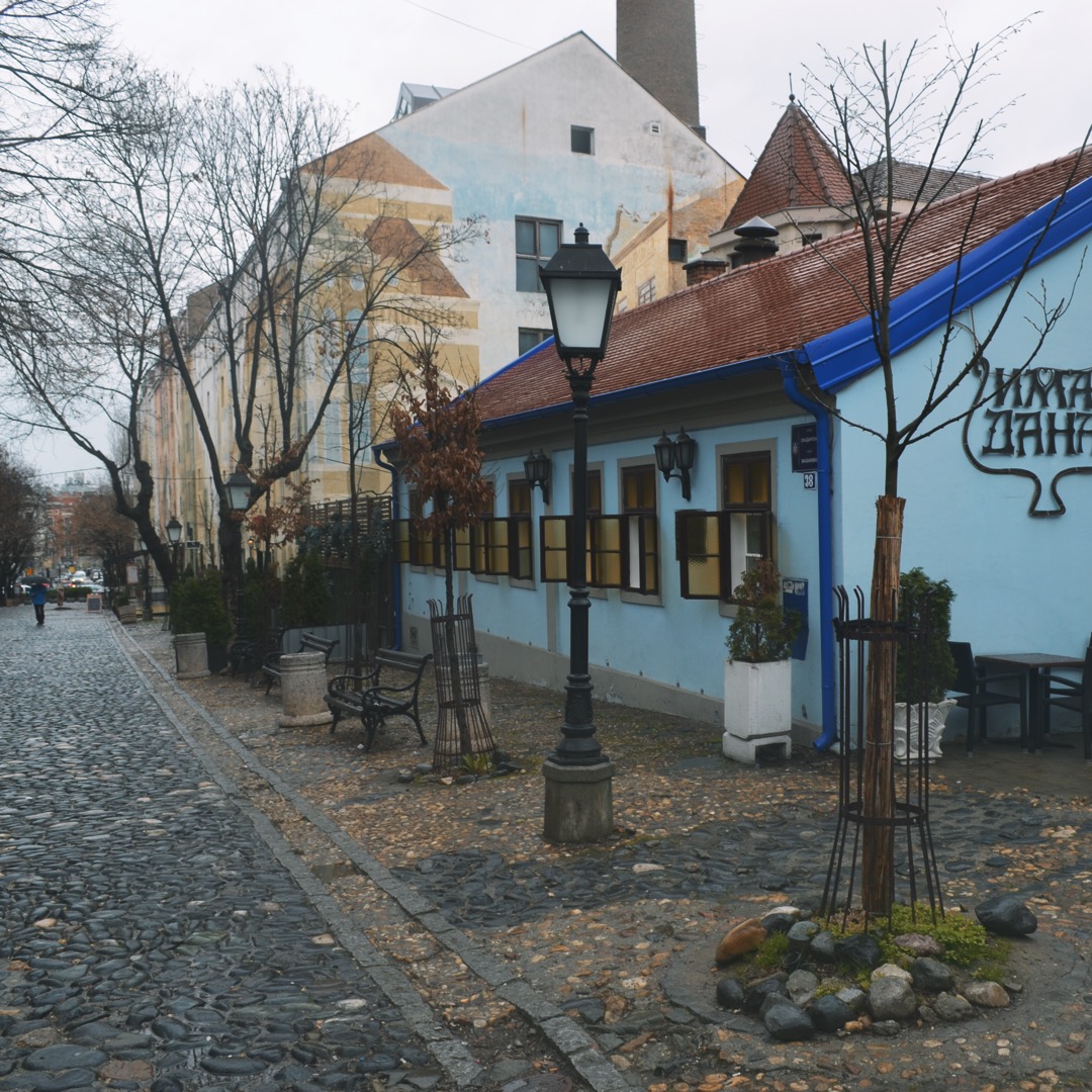 Things to do in Belgrade - The light blue facade of the historic Ima Dana restaurant with classic street lamps along the cobblestone street in Skadarlija, Belgrade.