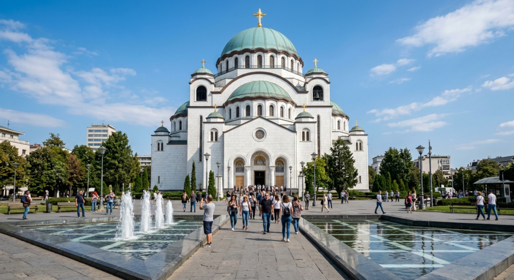 Temple of Saint Sava Belgrade Serbia Things to do in Belgrade - A sunny daytime photo of the Temple of Saint Sava in Belgrade, Serbia, viewed from the front plaza. Shows the white marble facade, turquoise dome, and visitors walking around the nearby fountain.