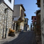 A narrow cobblestone street in Ano Poli (Upper Town), Thessaloniki, lined with historic houses and a vintage street lamp.