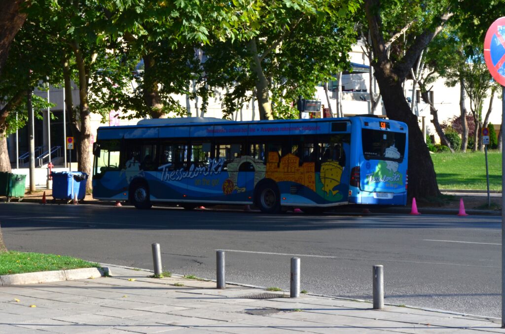 Blue Cultural Route Bus No. 50 in Thessaloniki, decorated with colorful illustrations of city landmarks, parked on a tree-lined street.
