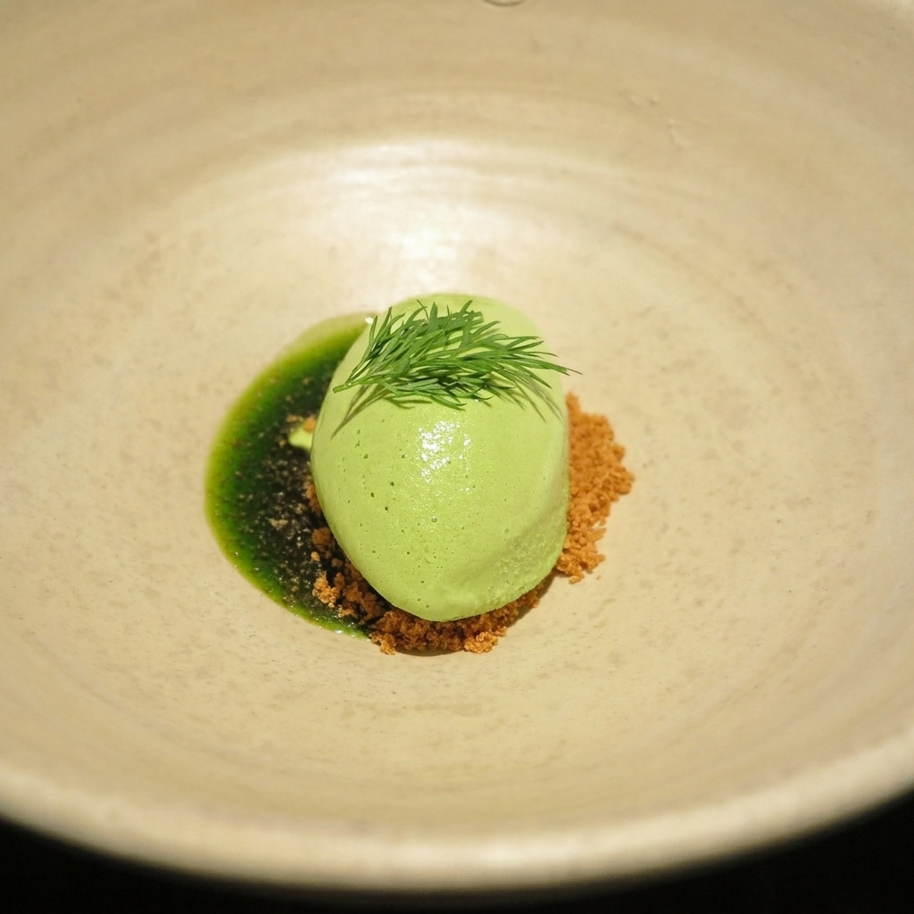 Od Urla - A quenelle of vibrant green dill sorbet topped with fresh dill sprig, served on crumble and green herb oil in a beige ceramic bowl.