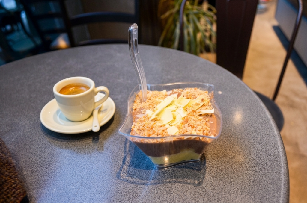 Evangelou Confectionary Kavala Greece Where to eat in Kavala? A cup of espresso next to a clear bowl of custom chocolate and vanilla profiterole dessert at Evangelou Confectionary in Kavala, Greece.