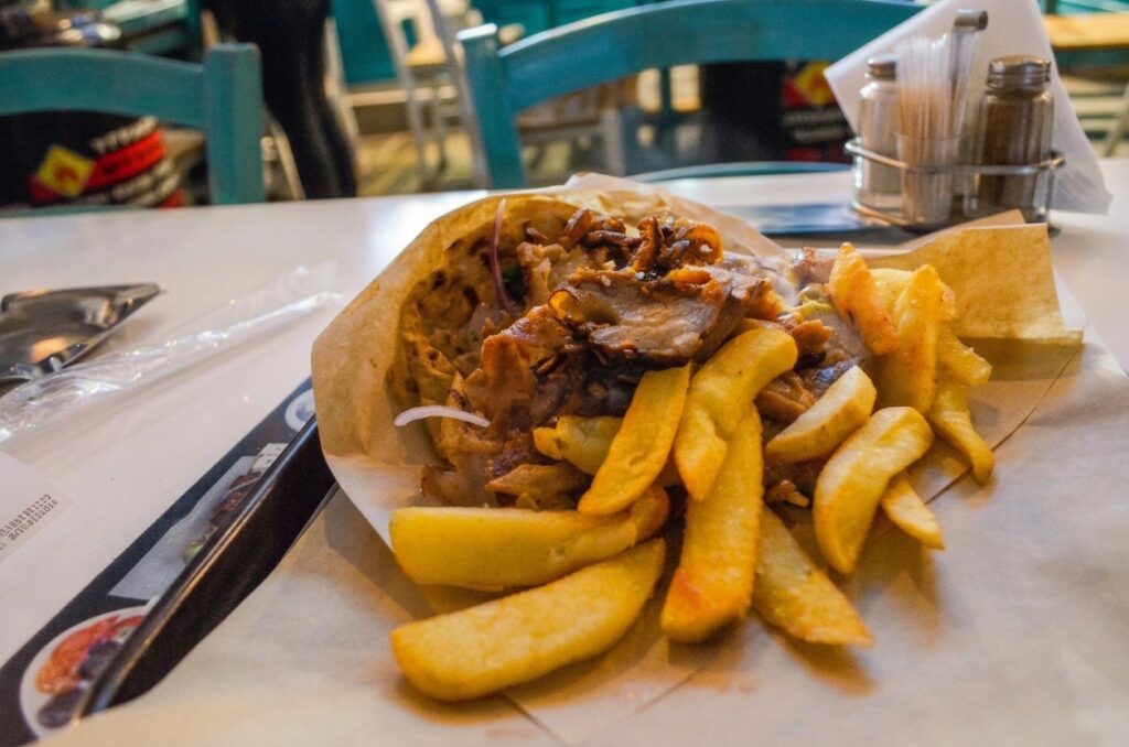 A detailed close-up of a large serving of Greek pork gyros meat and thick-cut fries, served in a paper wrap on a table at Mpoukia Mpoukia restaurant in Thessaloniki.